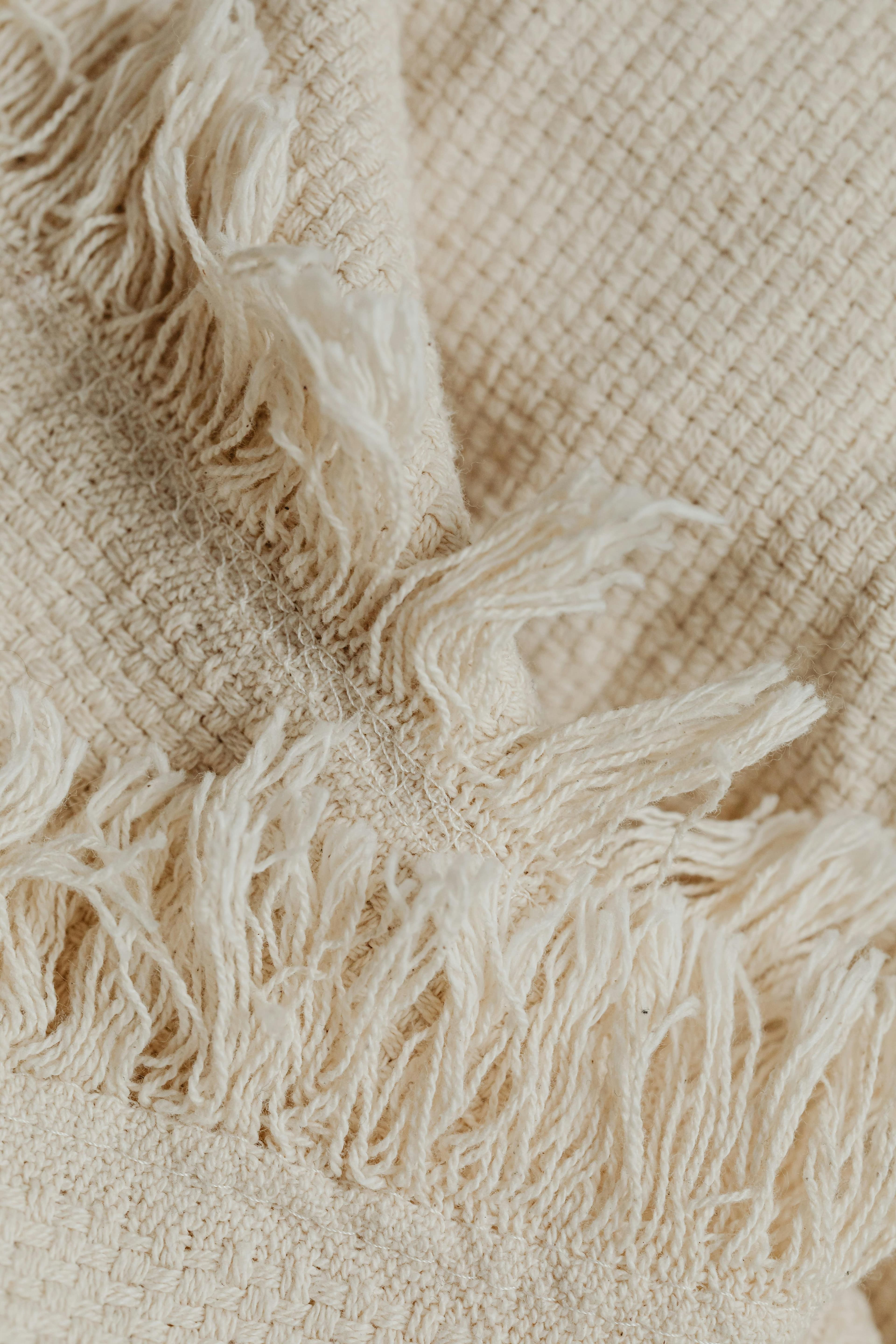 Détail d’un textile beige à franges, montrant un bord tissé à la main.